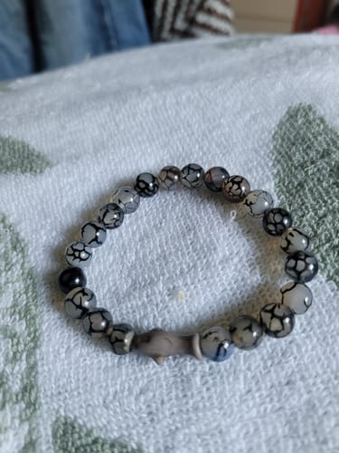 Customer's gray Voyage Bracelet with beaded texture and a small shark charm, resting on a white patterned cloth.