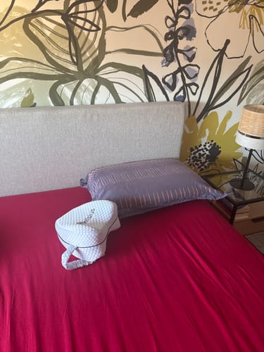Customer's Cellsius knee pillow with a white textured cover, resting on a bed with red sheets.