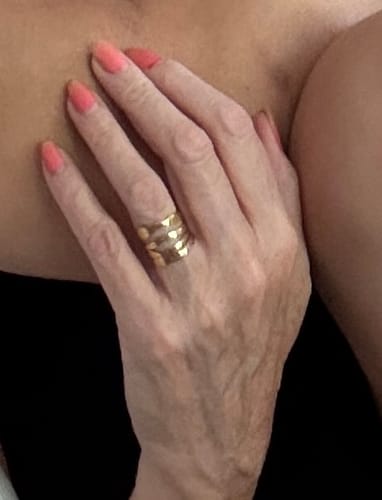 Reviewer's hand showing long-lasting Sunset Breeze gel nails in a coral pink color with a gold band ring.