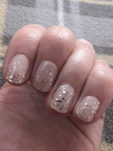 Customer's hand wearing Essentials nail strips with a light pink glitter gradient design after one week of wear.