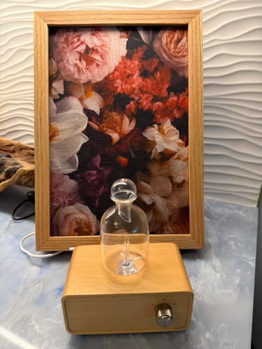 Customer's wooden Aura Nebulizer sits on a marbled surface in front of a floral print in a frame.