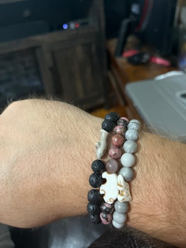 Customer's wrist wearing three layered beaded bracelets including shark and animal charm designs.