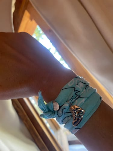 Reviewer's light blue Bracciale bandana con ciondoli di montagna, con un charm a forma di scarpone al polso.