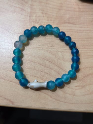 Customer's Voyage Bracelet featuring blue frosted beads and a white shark charm, resting on a flat surface.