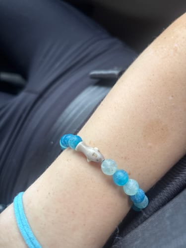 Customer's blue beaded Voyage Bracelet with a small shark charm worn on their wrist.