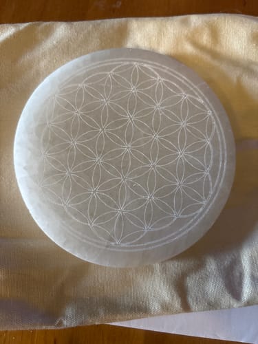 Customer's white circular Plateau Fleur de vie with a delicate engraved geometric pattern, resting on a cloth pouch.