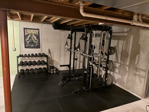 Customer's black RitFit M1 PRO Smith Machine set up in a basement gym with a dumbbell rack alongside it.