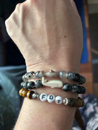 Customer's wrist wearing a stack of three beaded Voyage Bracelets featuring shark, whale, and letter beads.