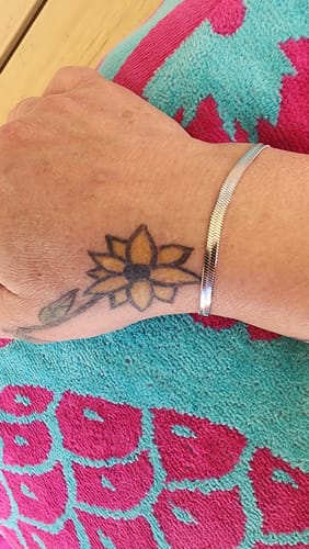 Reviewer's silver Sarya Snake Chain Bracelet on their wrist, featuring a sunflower tattoo.