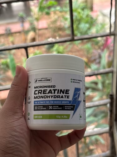 Reviewer's hand holding a white jar of Wellcore Micronised Creatine Monohydrate, Kiwi Kick flavor.