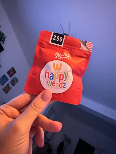 Customer's hand holding a red, 3.0g Happy Weedz THC-A flower pouch.
