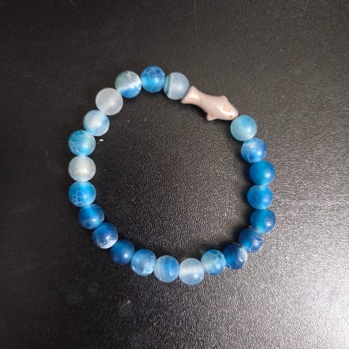 Customer's Voyage Bracelet featuring blue beaded stones and a small shark charm on a dark background.