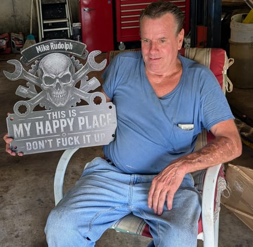 Customer's personalized metal sign held by a person in a garage setting.