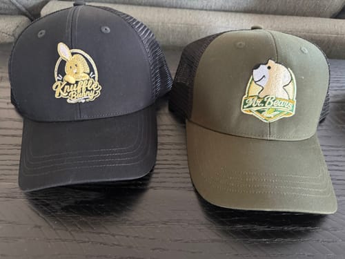 Customer's two Custom Embroidery hats, one black and one olive, sitting on a table.