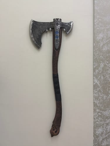 Customer's Ragnarok Kratos axe mounted on a plain wall, showing the detailed carved handle and metallic axe head.