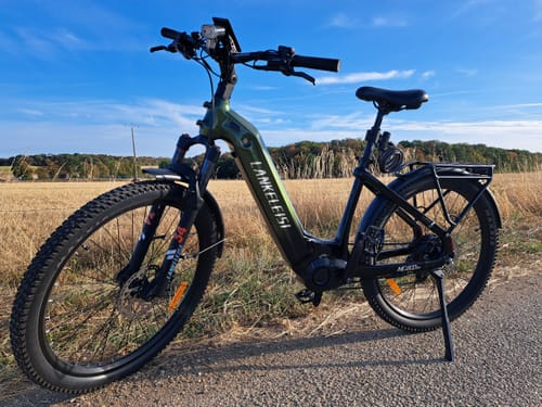 Customer's green Lankeleisi MG600 Lite electric trekking bike parked on a gravel path near a field.