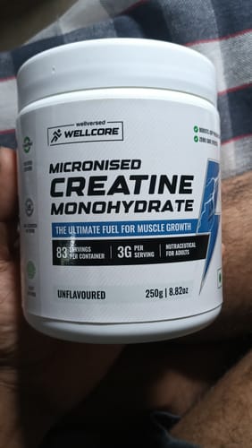 Customer's hand holding a white, round Wellcore Creatine Monohydrate container with bold blue text.