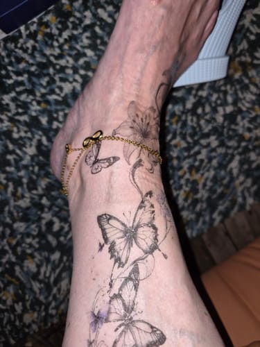 Customer's gold-colored Fußkettchen der Unendlichkeit with butterfly tattoos on the ankle.