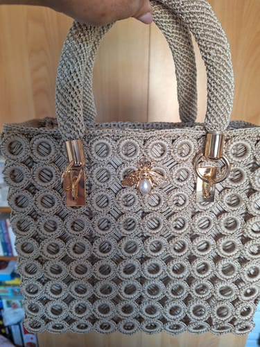 Customer's finished Garden Bee Crochet Bag Kit with pearl bee charm and gold hardware held by a hand.
