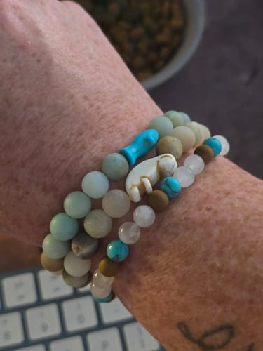 Customer's wrist wearing three Voyage Bracelets with colorful beads, including a shark-shaped charm.