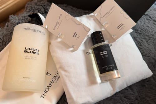 Customer's 50ml Fragrance & Body Wash bundle including perfume, body wash, and samples on a white cloth and gray rug.