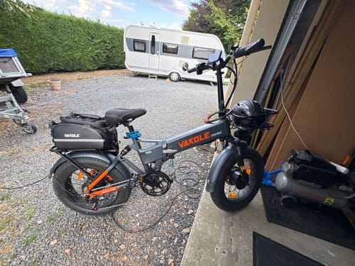 Customer's gray Vakole CO20 MAX folding bike parked on a gravel driveway with a travel trailer in the background.