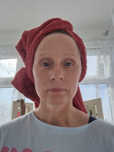 Customer's face after using Youth Boost, showing smooth and glowing skin with a red towel wrapped around her hair.