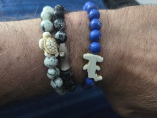 Customer's wrist wearing three different beaded bracelets, including a Voyage Bracelet with a shark charm.