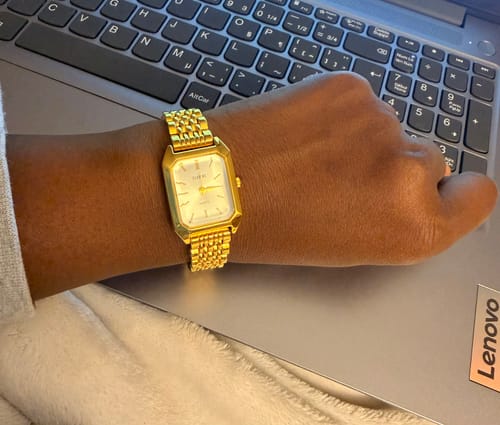 Customer's gold Claire De Mains watch worn on their wrist, resting on a laptop keyboard.