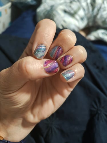 Reviewer's hand showing Gloss Top Coat manicure with colorful, marbled nail art designs.