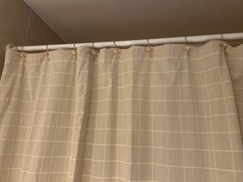 Customer's set de ganchos para cortina de baño con diseño de palmera dorada puestos en una cortina de tela beige.