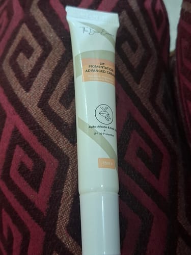 Customer's Advance Lip Pigmentation Cream in a slim beige tube, displayed against a dark patterned fabric background.