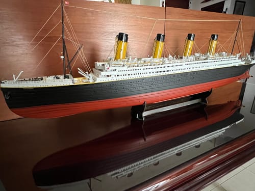 Customer's completed Titanic model ship sitting on a wooden stand with a visible reflection on the dark surface.