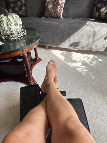 Customer's legs showing smooth skin after using the Body Serum, resting on a footrest in a living room.