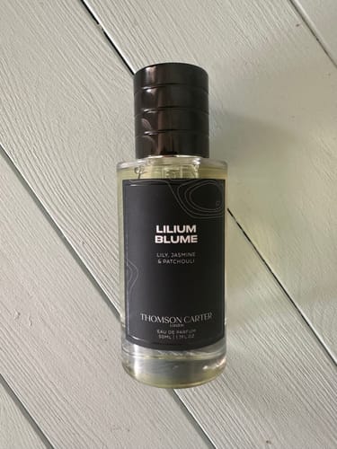 Customer's 50ml bottle of Lilium Blume Eau de Parfum with a black cap, standing on a white wooden surface.