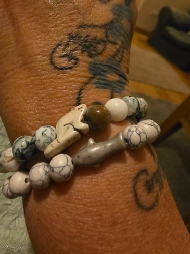 Customer's wrist wearing two Voyage Bracelets featuring a small animal charm and a shark charm with patterned beads.