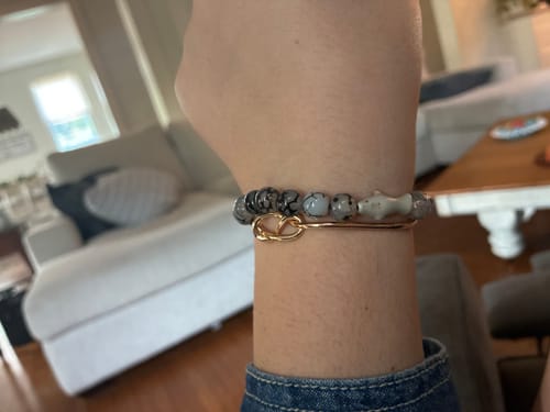 Customer's hand wearing the grey Voyage Bracelet, featuring a small shark charm and gold clasp.