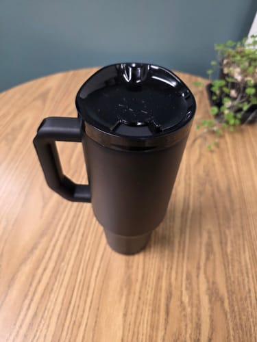 Customer's matte black Thicc Buddy 40oz tumbler with a closed lid sitting on a wooden table.