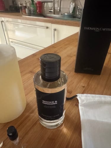 Customer's Smoke & Mirrors Eau de Parfum bottle, black box, and white drawstring bag on a wooden kitchen counter.