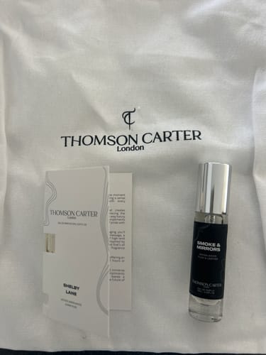 Customer's Shelby Lane perfume and Smoke & Mirrors perfume bottle on a white Thomson Carter branded fabric background.