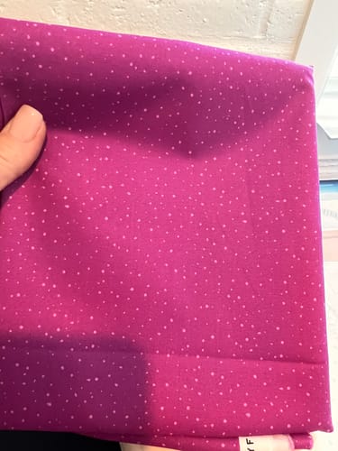 Reviewer's hand holding a piece of plum purple quilting fabric with small white polka dots.