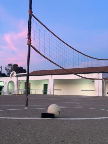 Reviewer's Enrforce Bluetooth Speaker placed on the ground by a volleyball court at sunset.