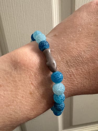 Customer's aqua blue Voyage Bracelet on wrist featuring a shark-shaped bead.
