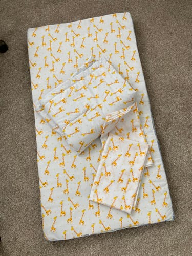 Customer's Giraffes on White Polycotton Fabric sewn into a soft cot quilt, folded on carpet.