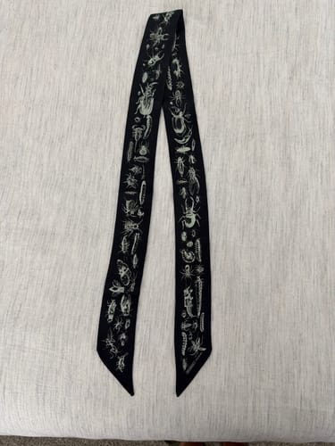 Customer's Crawlies skinny scarf, flat on a surface, featuring an intricate insect print on a black background.