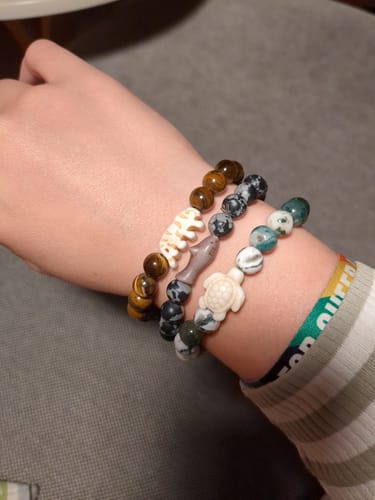 Customer's wrist wearing three beaded Voyage Bracelets featuring animal charms, including a turtle and a shark.