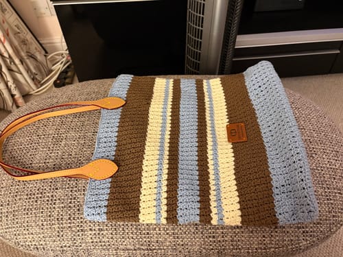 Customer's completed Sunday Tote Crochet Kit, featuring blue, brown, and cream stripes with tan leather straps.