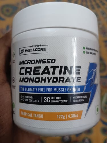 Customer's hand holding a white tub of Wellcore Micronised Creatine Monohydrate Tropical Tango.
