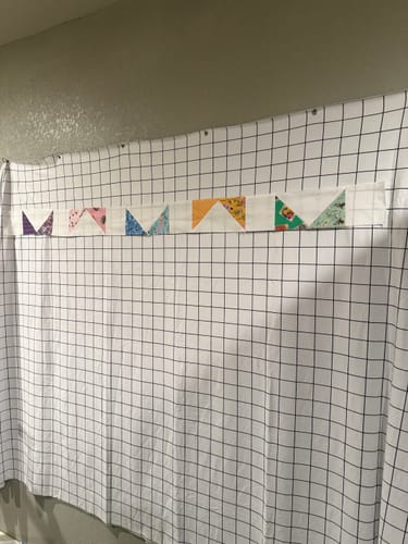 Reviewer's Flower Quilt kit pieces pinned to a grid-patterned design wall.