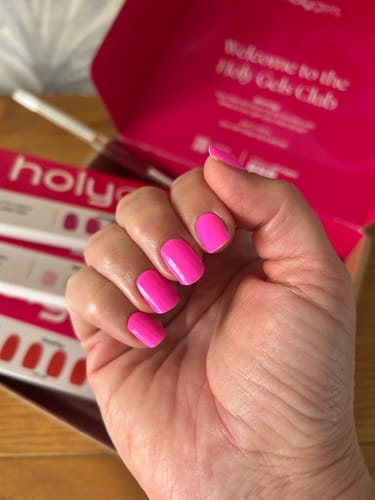 Customer's hand showing Flamingo colored Holy Gels nails, with the kit packaging visible in the background.